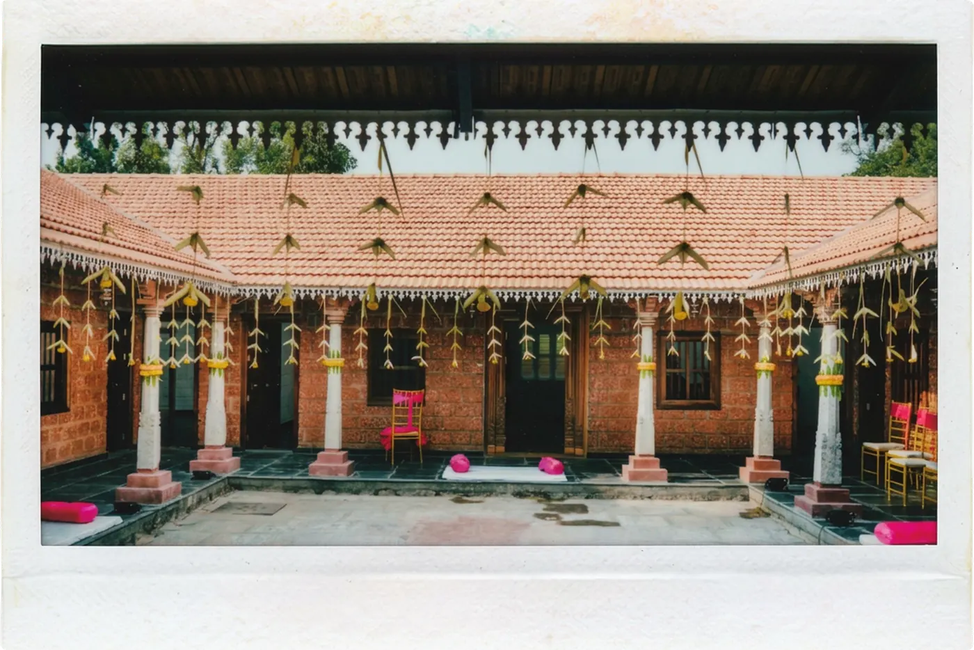 The courtyard at Tharavadu Mane, strung with marigold and mango-leaf garlands, with a tiled roof and carved pillars around an open central pool.